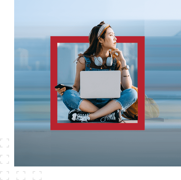 A woman sitting down with a laptop on her lap and a mobile phone in her right hand
